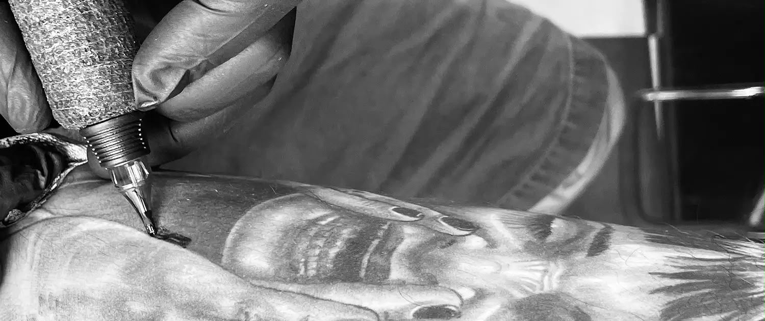 Gros plan sur un tatoueur au travail — machine et peau en noir et blanc